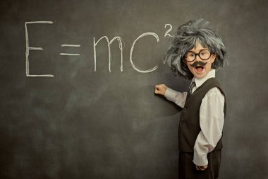 Alışılmışın dışında düşün. Gözlüklü, bıyıklı ve peruklu sevimli bir çocuk, küçük bir fizik profesörü gibi poz veriyor. Siyah karatahta arka planı. Eğitim ve erken kalkınma.