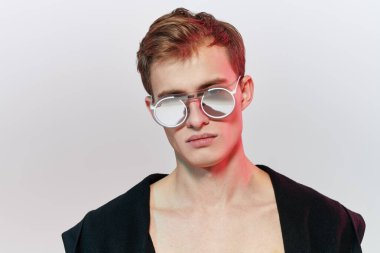 Siyah kapüşonlu ve şık güneş gözlüklü yakışıklı sarışın bir adamın portresi. Kendinden emin görünüyor. Gözlük modası. Beyaz bir arka planda stüdyo çekimi. Metin için boşluk.