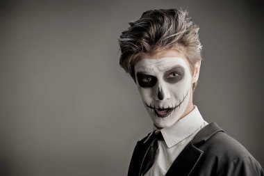 Stüdyoda gri arka planda poz veren iskelet kostümlü bir gencin portresi. Gençler için Cadılar Bayramı partisi. Metin için boşluk.