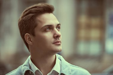 Paltolu yakışıklı, modern bir adam bulutlu bir günde bir şehir caddesinde duruyor ve gülümsüyor. İnsanlar ve duygular, yaşam tarzı.