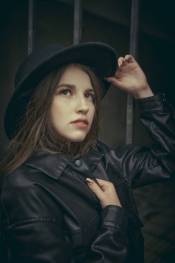 Güzel hippi kız bulutlu bir günde bir şehir caddesinde şapka ve deri ceket giyiyor. İnsanlar ve yaşam tarzı.