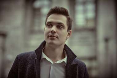 Paltolu yakışıklı, modern bir adam bulutlu bir günde bir şehir caddesinde duruyor ve hafifçe gülümsüyor. İnsanlar ve duygular, yaşam tarzı.