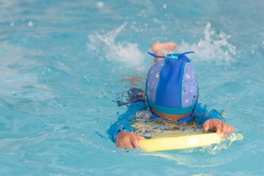 Küçük kız yüzme tahtasıyla havuzda yüzmeyi öğreniyor..