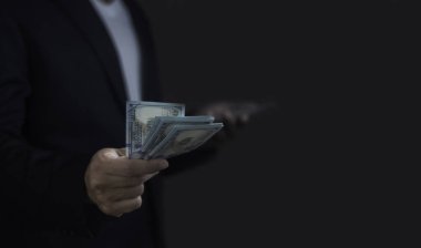 Bir adam elinde bir yığın yeşil banknot tutuyor. Takım elbise ve kravat takıyor.