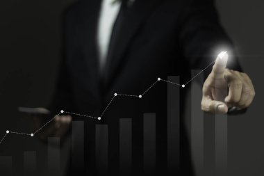 Takım elbiseli bir adam ekrandaki grafiği gösteriyor. Grafik, bir şirketin kârını veya hisse senedi eğilimini temsil edebilecek sayılarda istikrarlı bir artış gösteriyor.
