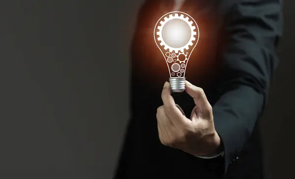 Adamın biri üzerinde dişliler olan bir ampul tutuyor. Yenilik ve yaratıcılık kavramı