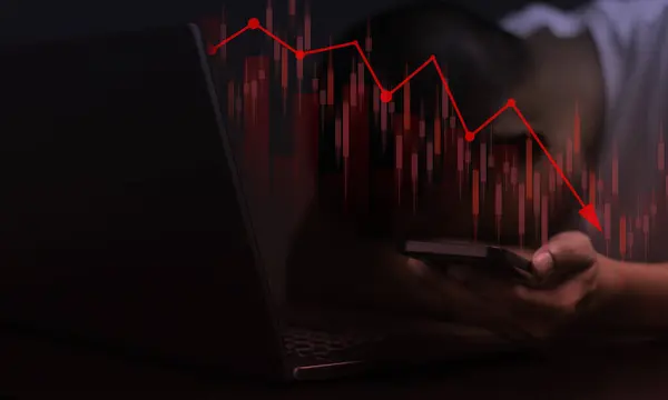 Adamın biri elinde telefon olan bir dizüstü bilgisayara bakıyor. Telefon ekranda aşağı yönlü bir eğilim gösteriyor. Adam durumdan endişe ediyor.