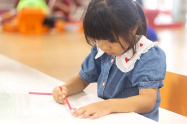 Şirin küçük kız renkli kalemle resim çizip boyamakla meşgul..