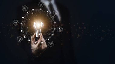 Koyu arkaplana karşı ekoloji kavramına sahip parlak ampulü tutan iş adamı.