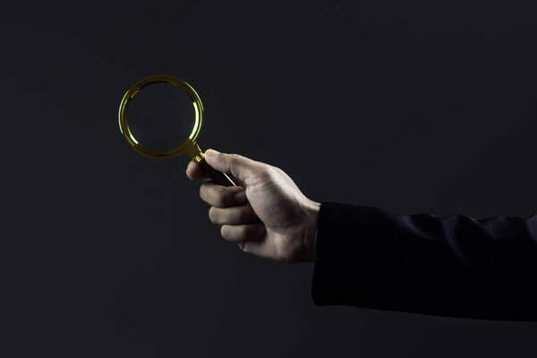 Close-up hand of businessman use magnifying glass against dark background.