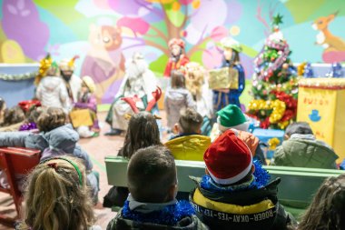 The three kings visiting children in a children's school, christian tradition, christmas festival in school, unrecognizable people, the background out of focus.