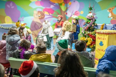The three kings visiting children in a children's school, christian tradition, christmas festival in school, unrecognizable people, the background out of focus.