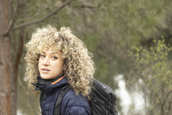 Портрет блондинки-альпинистки с вьющимися волосами, смотрящей в камеру и улыбающейся