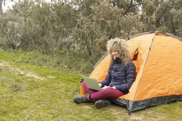 Kıvırcık Sarı Saçlı Dağcı Kadın Kamplarında Turuncu Çadırıyla Bilgisayarına Telgraf Telifsiz Stok Imajlar