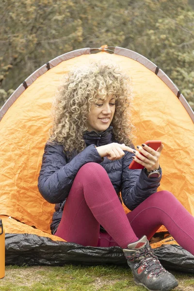 Kıvırcık Sarı Saçlı Dağcı Kadın Kamplarında Turuncu Çadırında Akıllı Telefonunu Stok Fotoğraf
