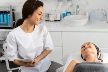 Çekici, yaşlı bir kadının portresi. Yatakta uzanıyor ve güzellik uzmanına gülümseyen bir şekilde bakıyor. 