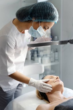 Masözün kapanışı, yaşlı kadın hasta yüzünü özel bir lamba altında dikkatle inceliyor. Kadın, özel koltukta uzanırken zevkle gözlerini kapadı. 