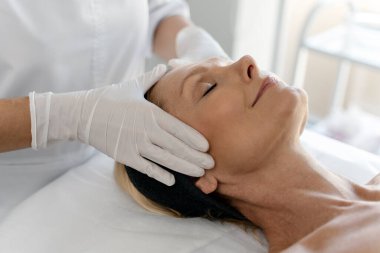 Profesyonel terapist tarafından yapılan yumuşak yüz masajı ile hoş bir güzellik prosedürü. Olgun kadın gözleri kapalı yatıyor. 