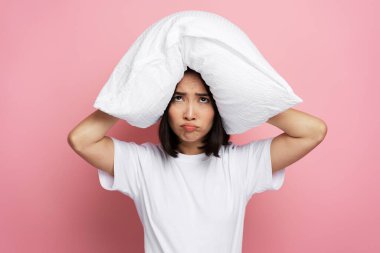 Sinirli ve sinirli kadın, sabahları gürültü yüzünden kulaklarını yastıkla kapatıyor. Alarmlı saat ya da gürültülü komşunun rahatsız ettiği uykusuz kadının yakın plan portresi. Uykusuzluk, stres ve kulak çınlaması kavramı 