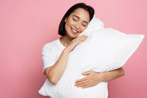 目を閉じてピンク色の背景に隔離された眠っている豪華な女の子抱擁枕を満足させました 就寝時のコンセプト — ストック写真