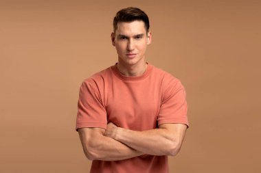 Mutlu beyaz adam portresi ayakta, kameraya pozitif bir gülümsemeyle bakıyor. Bej arka planda izole edilmiş kapalı stüdyo çekimleri