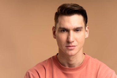 Mutlu beyaz adam portresi ayakta, kameraya pozitif bir gülümsemeyle bakıyor. Bej arka planda izole edilmiş kapalı stüdyo çekimleri