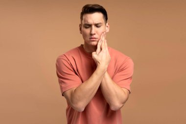 Diş sorunları. Ağrıyan yanağa baskı yapan sağlıksız bir adamın portresi, akut diş ağrısı, periodontal hastalık, çürük ya da çene ağrısı. Bej arka planda izole edilmiş kapalı stüdyo çekimi 