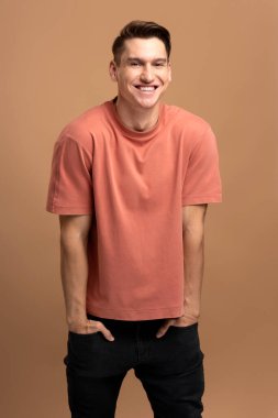 Mutlu beyaz adam portresi ayakta, kameraya pozitif bir gülümsemeyle bakıyor. Bej arka planda izole edilmiş kapalı stüdyo çekimleri