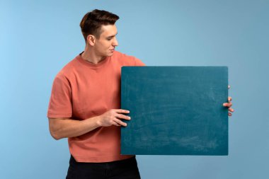 Boş afiş taşıyan yakışıklı bir adam, ona bakıyor. Olumlu ve mutlu adam kendine güvenen bir gülümseme ile ayakta ve gülümsüyor. Reklam kavramı 