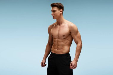 Güçlü atletik erkek fitness modeli çıplak gövde ile poz veriyor. Mavi arka planda 6 paket karın kasları görünüyor. Spor konsepti 