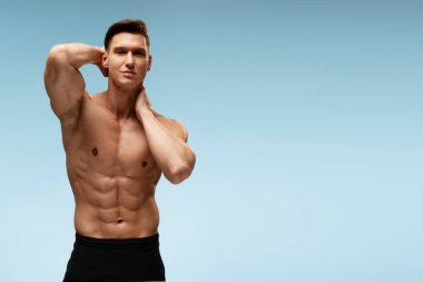 Stüdyoda kaslı vücudunu mavi arka planda gösteren genç bir vücut geliştirici. Sportif insanlar konsepti 