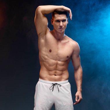 Çıplak gövdesi neon dumanlı siyah arka planda olan genç atletik bir adam. Sportif insanlar konsepti 