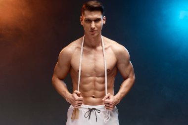 Neon kaplamalı çıplak gövdeli atletik bir adam. Reklam fitness antrenörü boynunda ip atlayarak gülümsüyor. 
