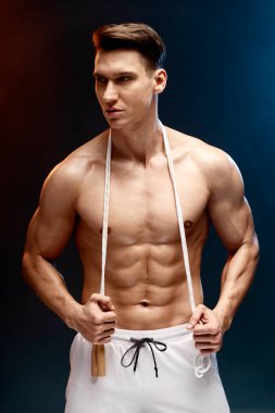 Neon kaplamalı çıplak gövdeli atletik bir adam. Reklam fitness antrenörü boynunda ip atlayarak gülümsüyor. 