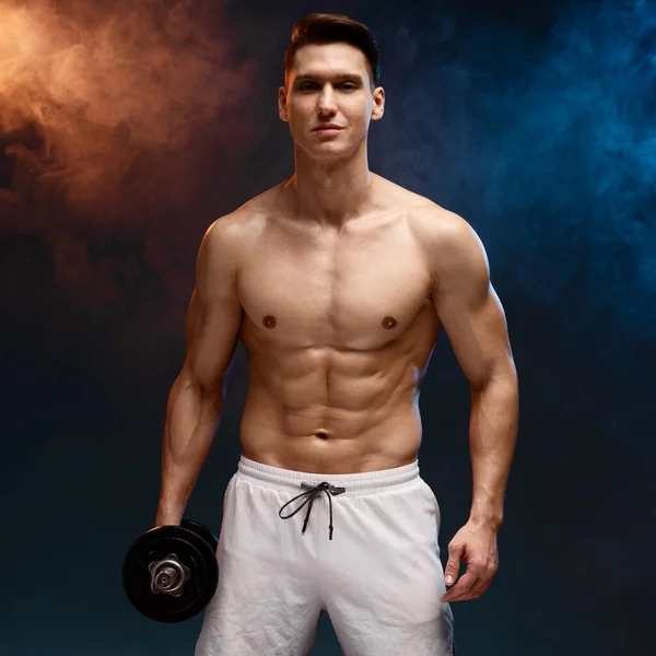 Portrait of masculine young man holding dumbbell isolated on black background. Naked torso of young man is perfect, doing cross fit workout, training, bodybuilding concept