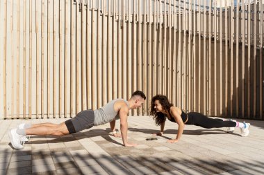 Morning workout concept. Happy athlete couple standing at plank pose together and making push ups exercise during sport training outdoors 