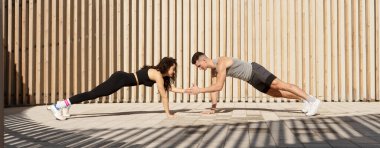 Young sportive couple in plank pose exercising together on sport street playground, widescreen. Healthy lifestyle and street sport concept 