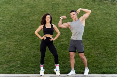 Strong man showing biceps and posing near fit woman. Sportive people standing over grass background. Sport and recreation concept. Stock photo 