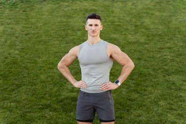 Horizontal shot of strong man with fit body posing to the camera and leading healthy lifestyle. Grass background. Stock photo