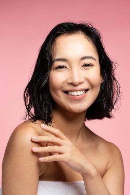 Vertical view of the young pretty woman touching healthy skin on shoulder. Beautiful asian brunette female person posing after shower. Skin care concept