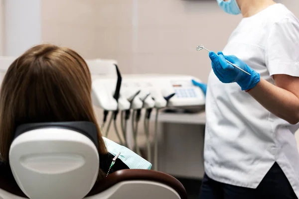 Female patient sitting in the dental chair, the dentist is holding a dental mirror in his hand, he will examine the patient\'s teeth. Professional dental treatment.