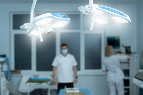 Closeup , operating lamp on in operating room, medical staff, doctor and nurse on blurred background. Modern operating room, preparation for surgery.