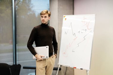 Bilgisayarı kullanan yakışıklı bir adam, modern ofiste çizelgenin yanında duruyor. İş yerinde çalışan bir işadamı