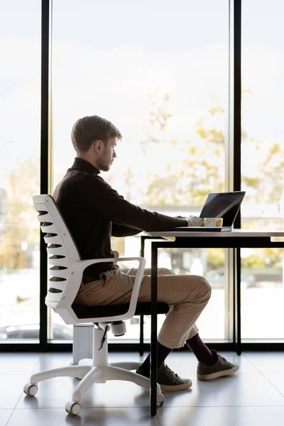 매력적 사람은 노트북으로 일하고 의자에 앉아서 기술을 합니다 사무실 평상복 스톡 사진