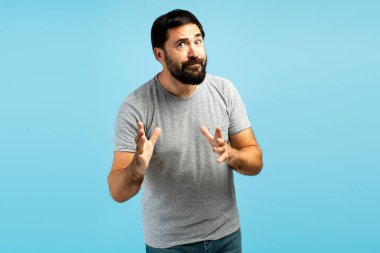 Elleriyle hareket eden kafası karışmış olgun bir adam, canlı bir mavi zemine karşı yanlış anlaşılma ya da kafa karışıklığını ifade ediyor.