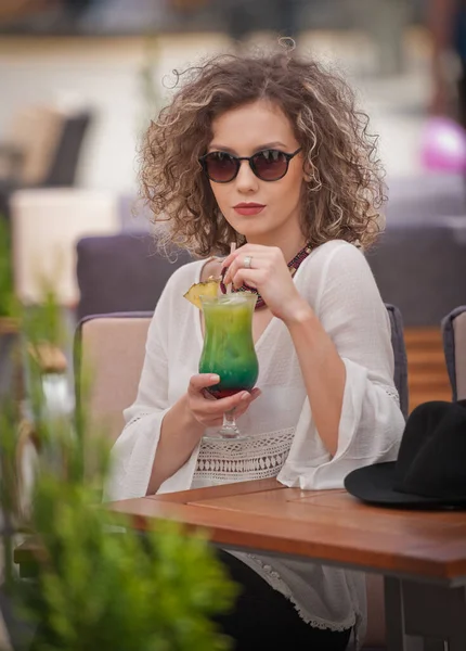 快乐的黑发女孩太阳镜坐在公园里 喝一杯冷绿汁而微笑到距离 年轻漂亮的女人喝果汁穿着一件白衬衫坐在板凳上 — 图库照片