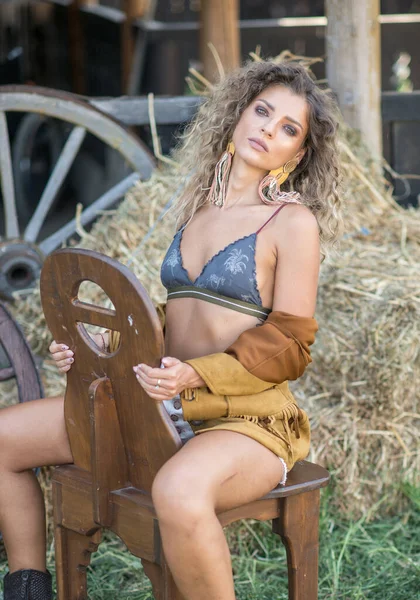 一个长腿 棕色靴子的性感女孩坐在农场的木椅上 在西部的户外场景中 一个英俊的女孩穿着漂亮的身体 流行的金发模特 — 图库照片