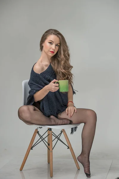迷人的女人穿着黑色的裤袜和长长的腿摆出一副挑战的架势 手里拿着杯子 经典的闺房场景 室内情色照片 有一头卷曲长发的性感年轻女子坐在椅子上 — 图库照片