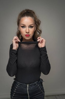 Siyah bluzlu ve kırmızı dudaklı çekici bir kadın arka planda meydan okuyor. Klasik yatak odası sahnesi. Uzun kıvırcık saçlı ve kameranın önünde siyah kot giyen şehvetli genç bir kadın.