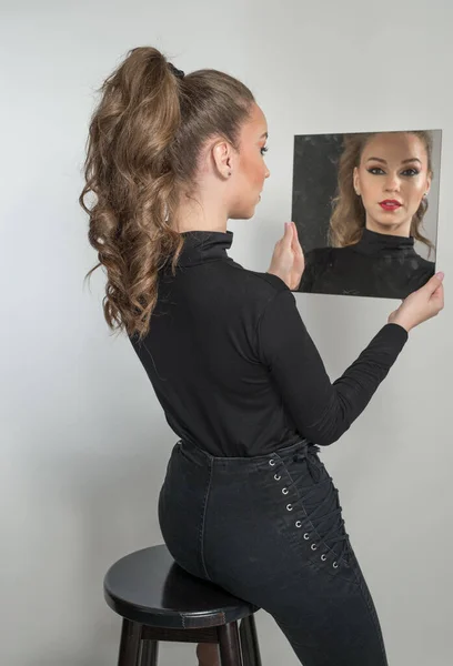 黒のブラウスと赤い唇の魅力的な女性は 背景の前に鏡を見てください ブドアのシーンだ カメラの前で身に着けている長い巻き毛と黒のジーンズを持つ官能的な若い女性 — ストック写真